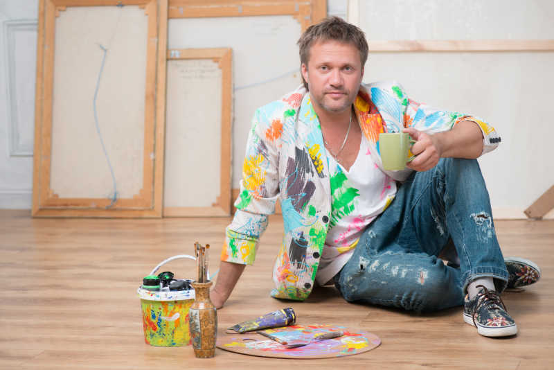 拿着茶杯坐在画室地板上的男人