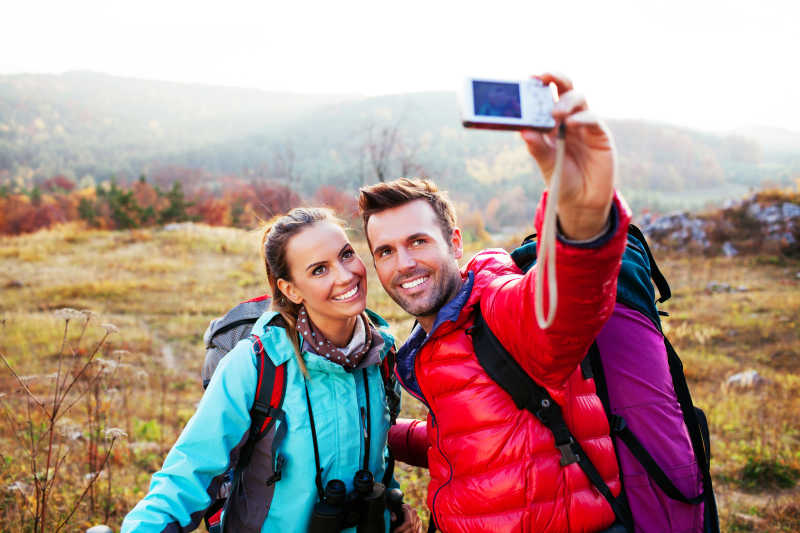 年轻情侣带背包户外用相机自拍