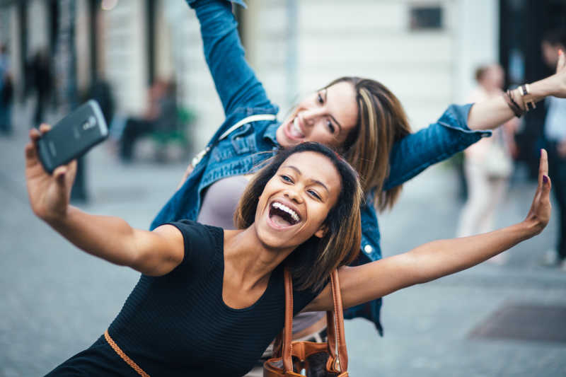 两个年轻女孩在户外街头用智能手机自拍