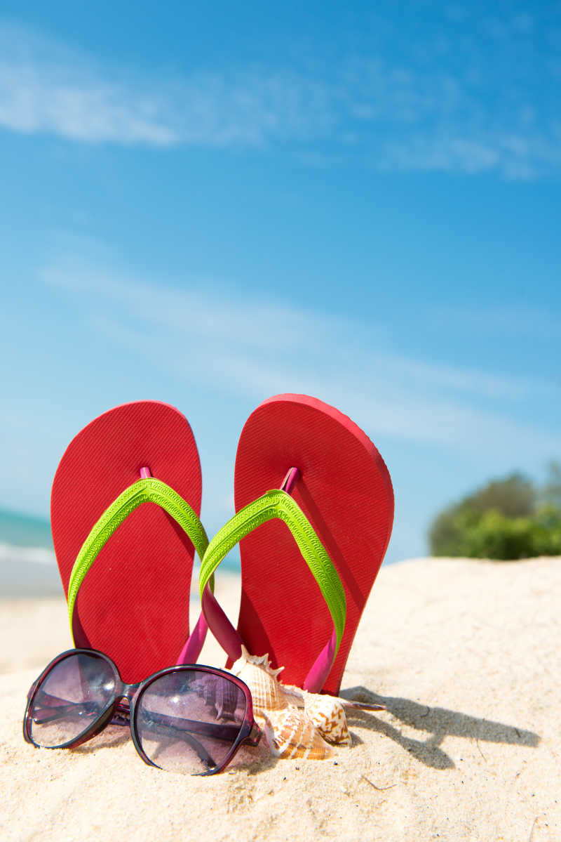 沙滩上的红色拖鞋和太阳镜