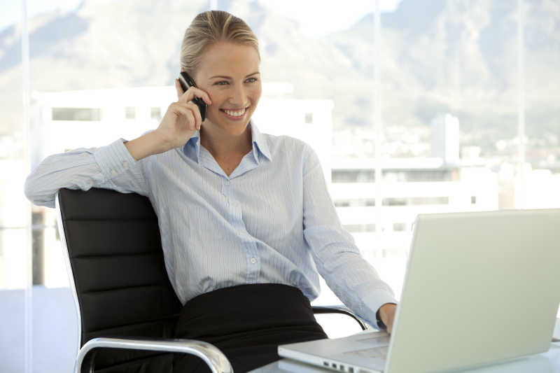 漂亮的女商人坐在电脑前打电话