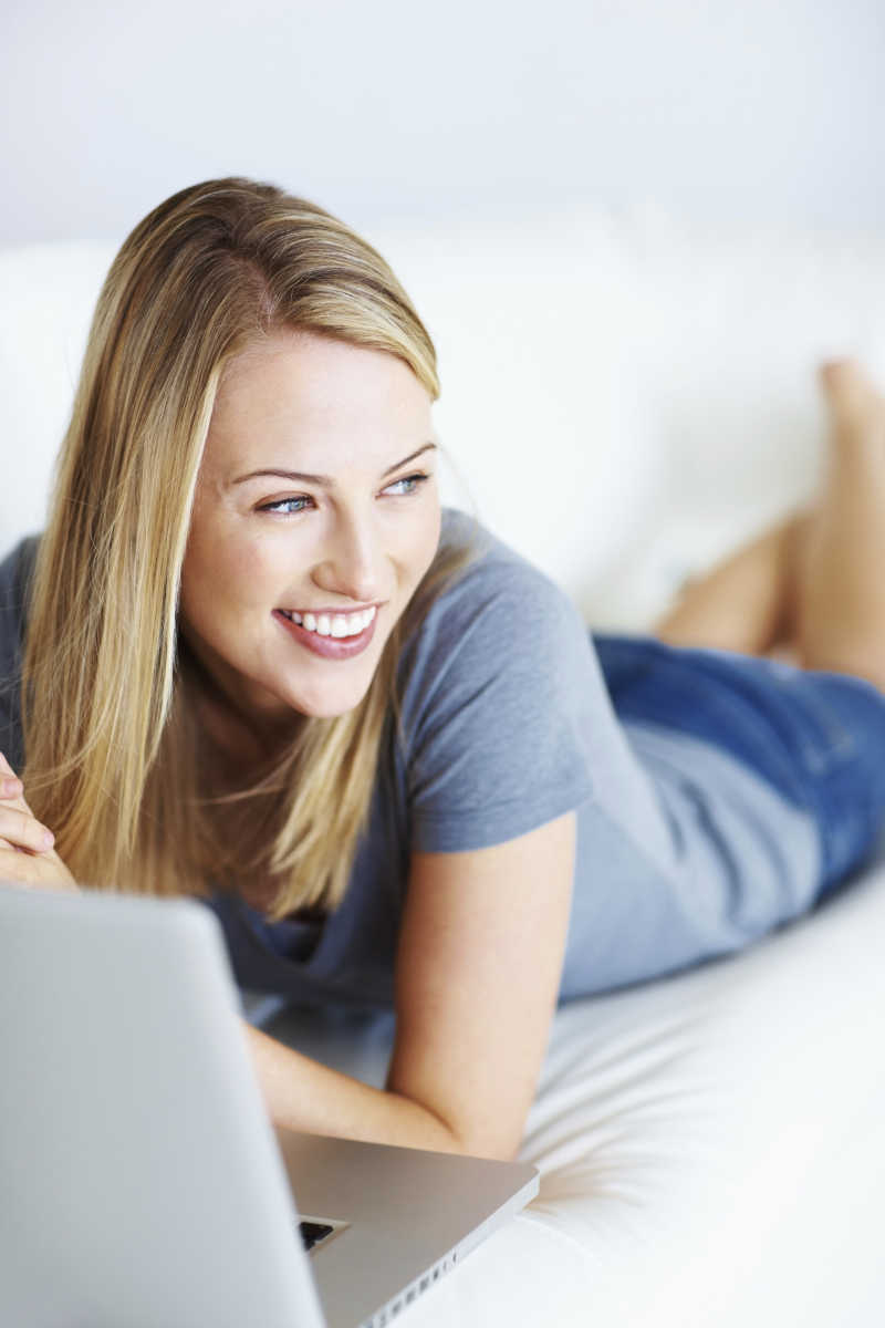 年轻女子趴在沙发上使用笔记本电脑
