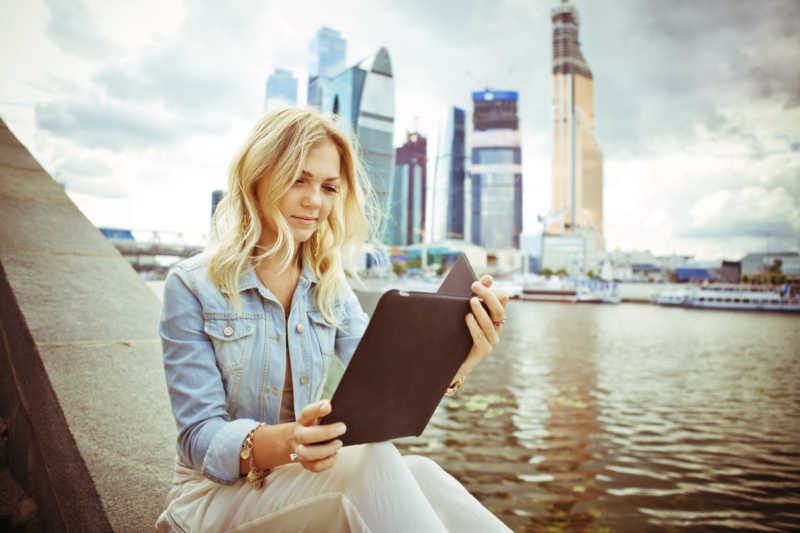 莫斯科国际商务中心附近一位年轻貌美的女子坐在户外使用数码平板电脑