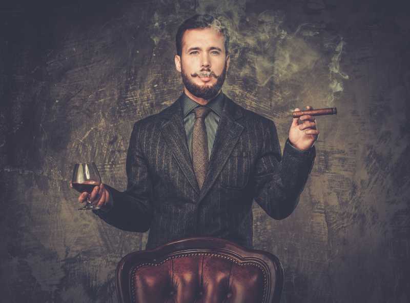 穿着西装的胡子男人拿着一杯饮料和雪茄