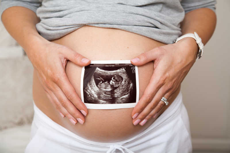 拿着B超照片放在肚子上的孕妇
