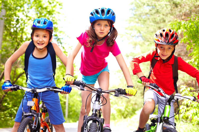 戴着儿童安全帽和手套骑自行车的三个儿童