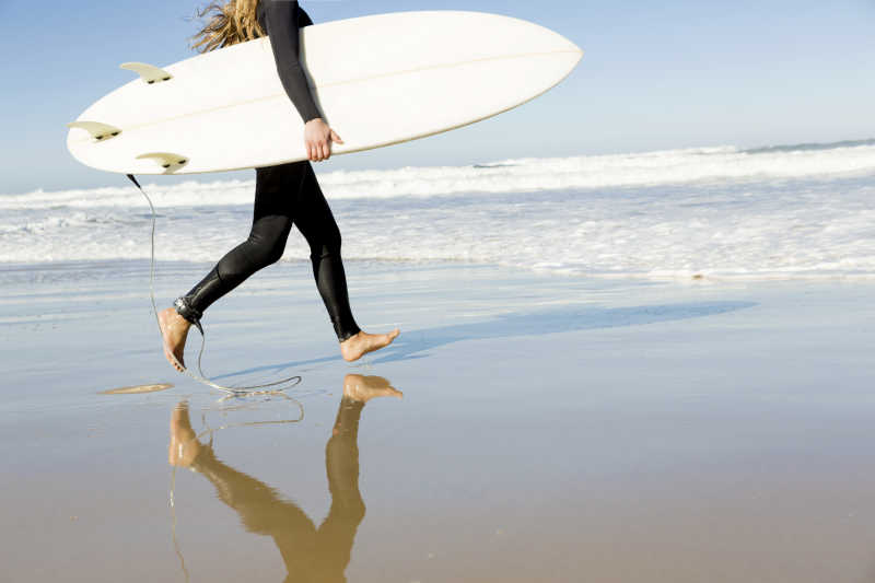 拿着冲浪板赤脚走在沙滩上的人