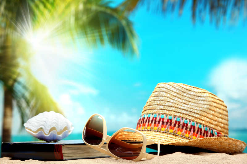 明媚天气里放在沙滩上的帽子和墨镜