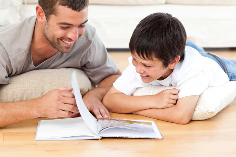 可爱的男孩在地板上和父亲一起读书