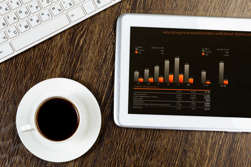 桌上放有图表和咖啡杯以及一个平板电脑