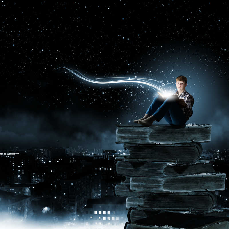 星空下坐在厚厚的书籍上看书的男孩