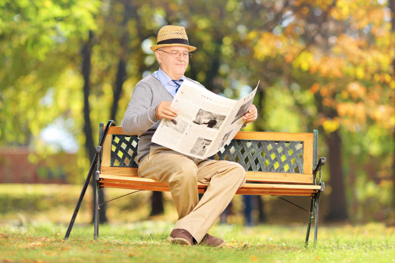 在公园长凳上看报纸的老年男性