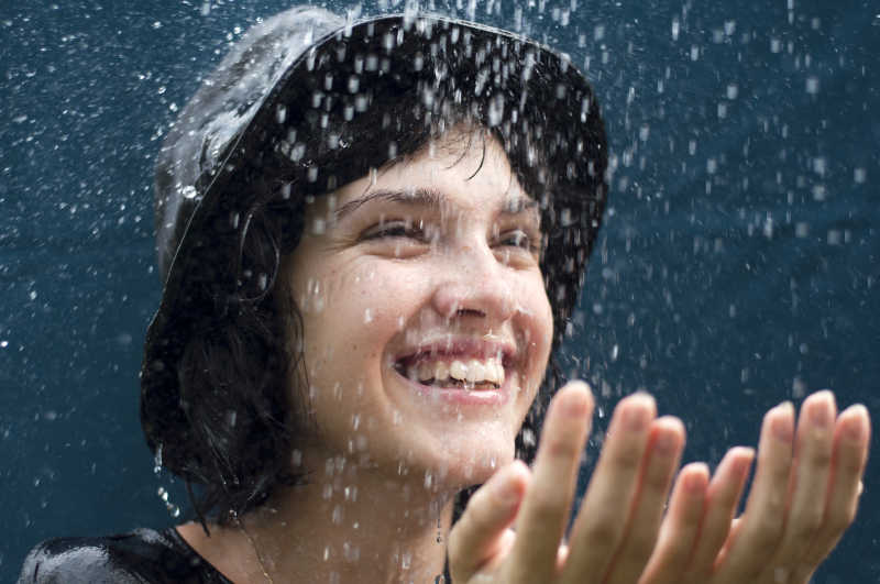 戴着帽子淋雨的女孩用双手接雨水