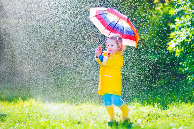 穿着黄色防水外套和雨靴的儿童拿着雨伞在玩耍