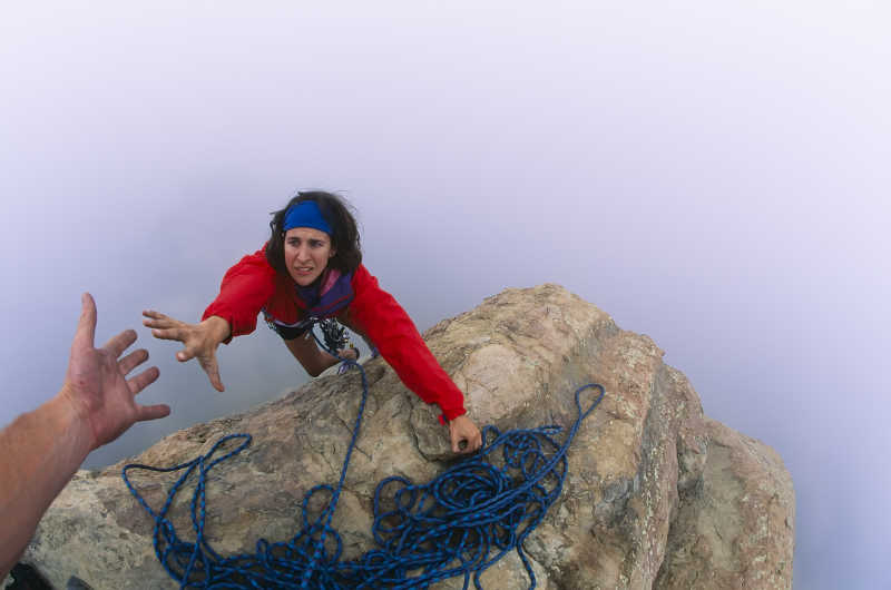 山顶上的攀岩者向伙伴伸出援助之手