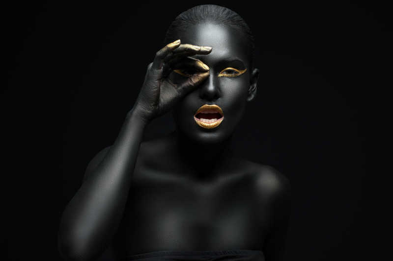 黑色背景上全身涂满黑色颜料的女人把手放在眼睛上
