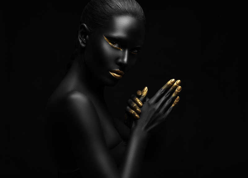 黑色背景上全身涂满黑色和金色颜料的女人