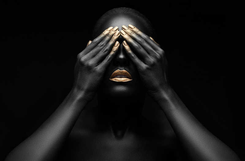 黑色背景上全身涂满黑色颜料的女人用双手捂着眼睛