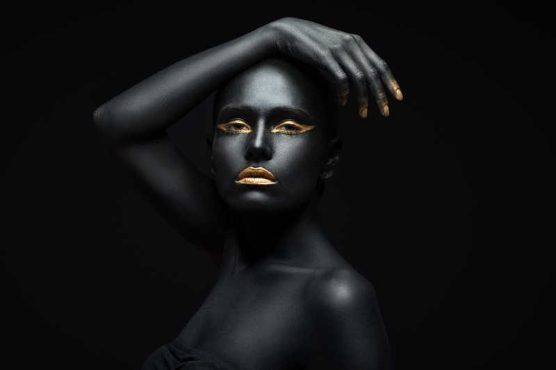 黑色背景上全身涂满黑色颜料的女人把手搭在头顶