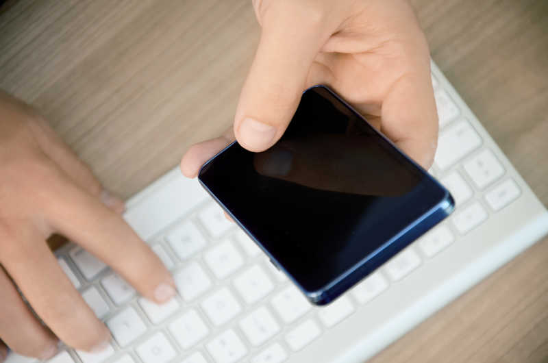 使用移动智能手机和电脑的年轻商人