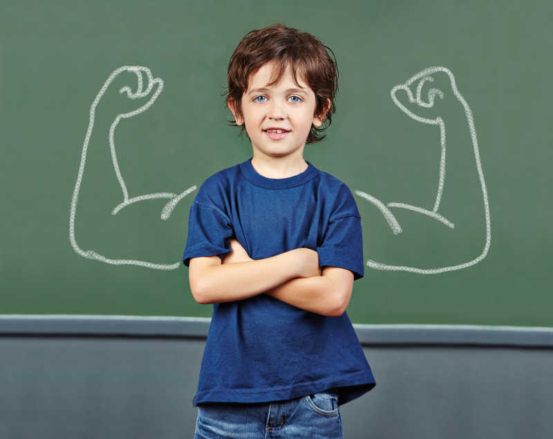 小男孩在黑板为自己画上肌肉强壮的双臂