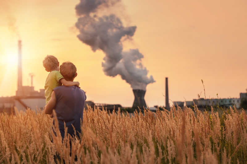 父亲和儿子看日落时旁边的化学工厂排放出浓浓的黑烟