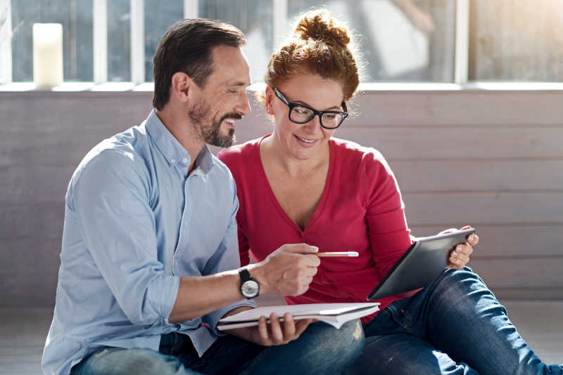 一同坐在地板上拿着笔记本电脑的夫妇做笔记