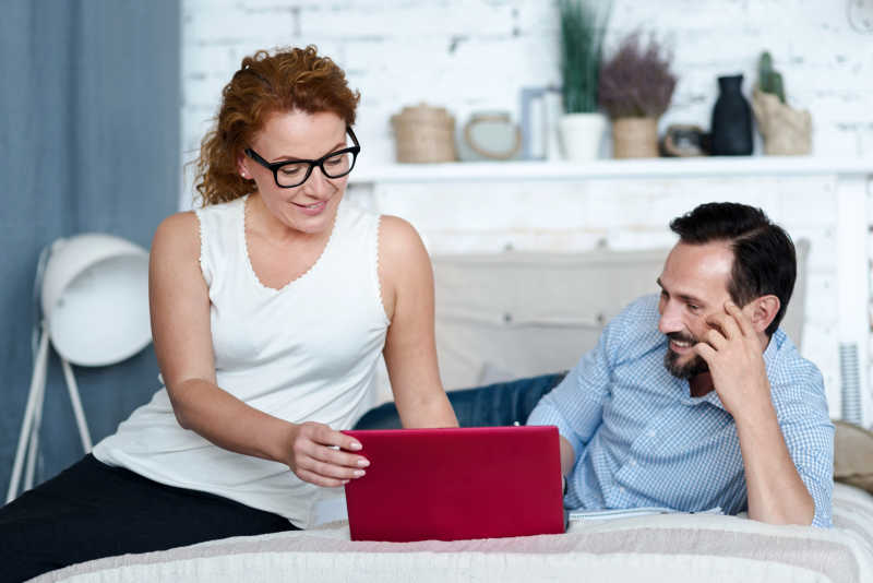 坐在床上拿着笔记本电脑的妻子和面带笑容的丈夫