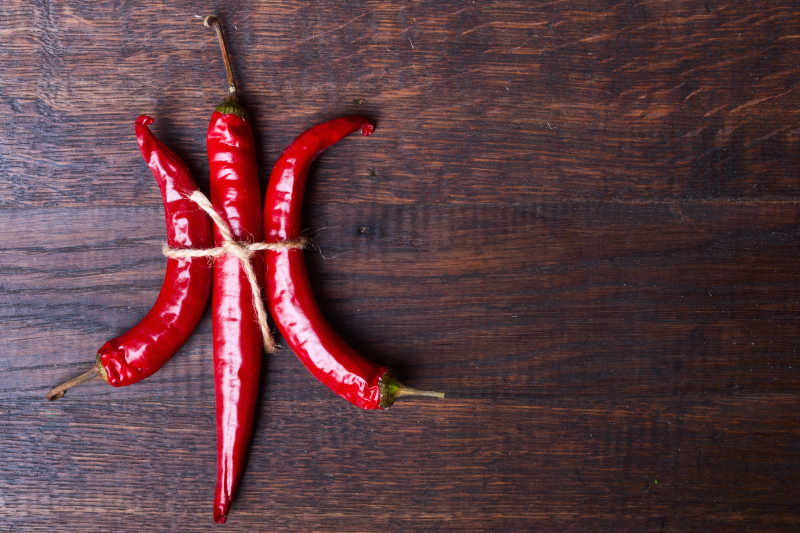 木桌上的用绳子绑着的三个红辣椒