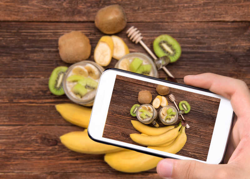 手拿智能手机拍摄香蕉猕猴桃沙冰