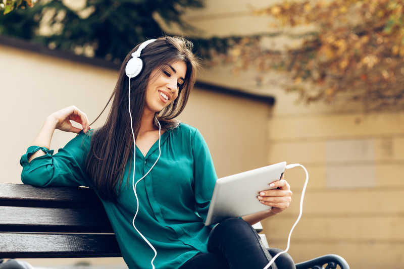 公园里拿着平板电脑欣赏音乐的年轻女子