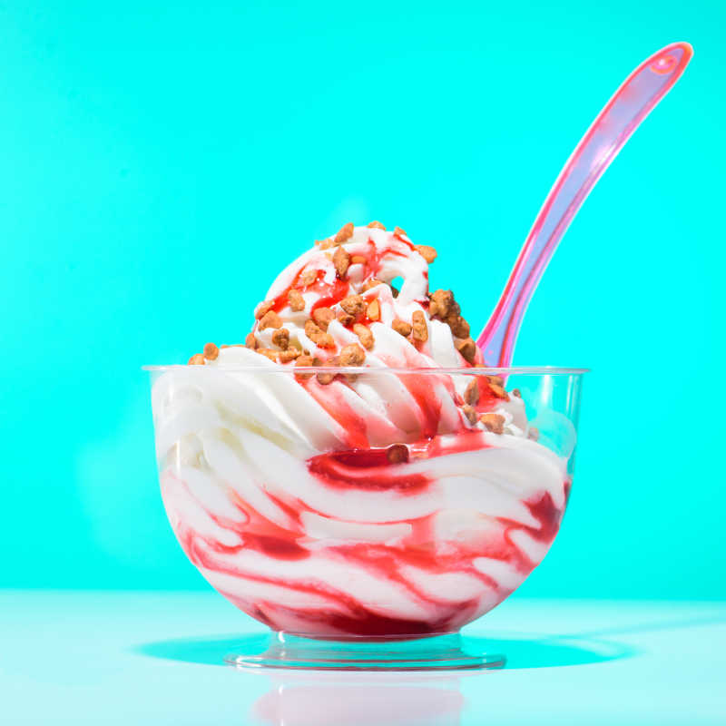 在蓝色背景的美味的草莓圣代冰淇凌在粉红色的塑料勺子