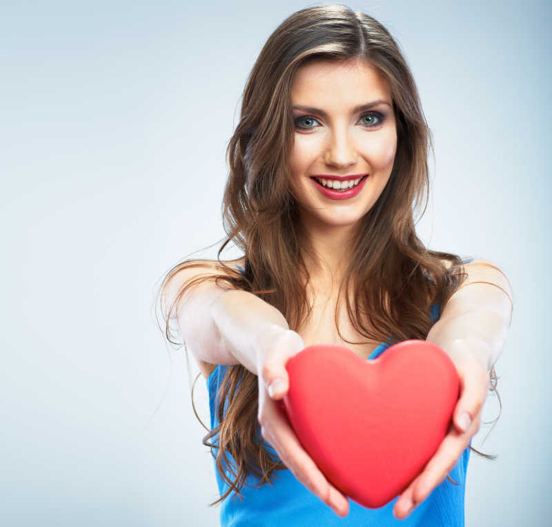 年轻的快乐女人抱着象征爱的红色的心