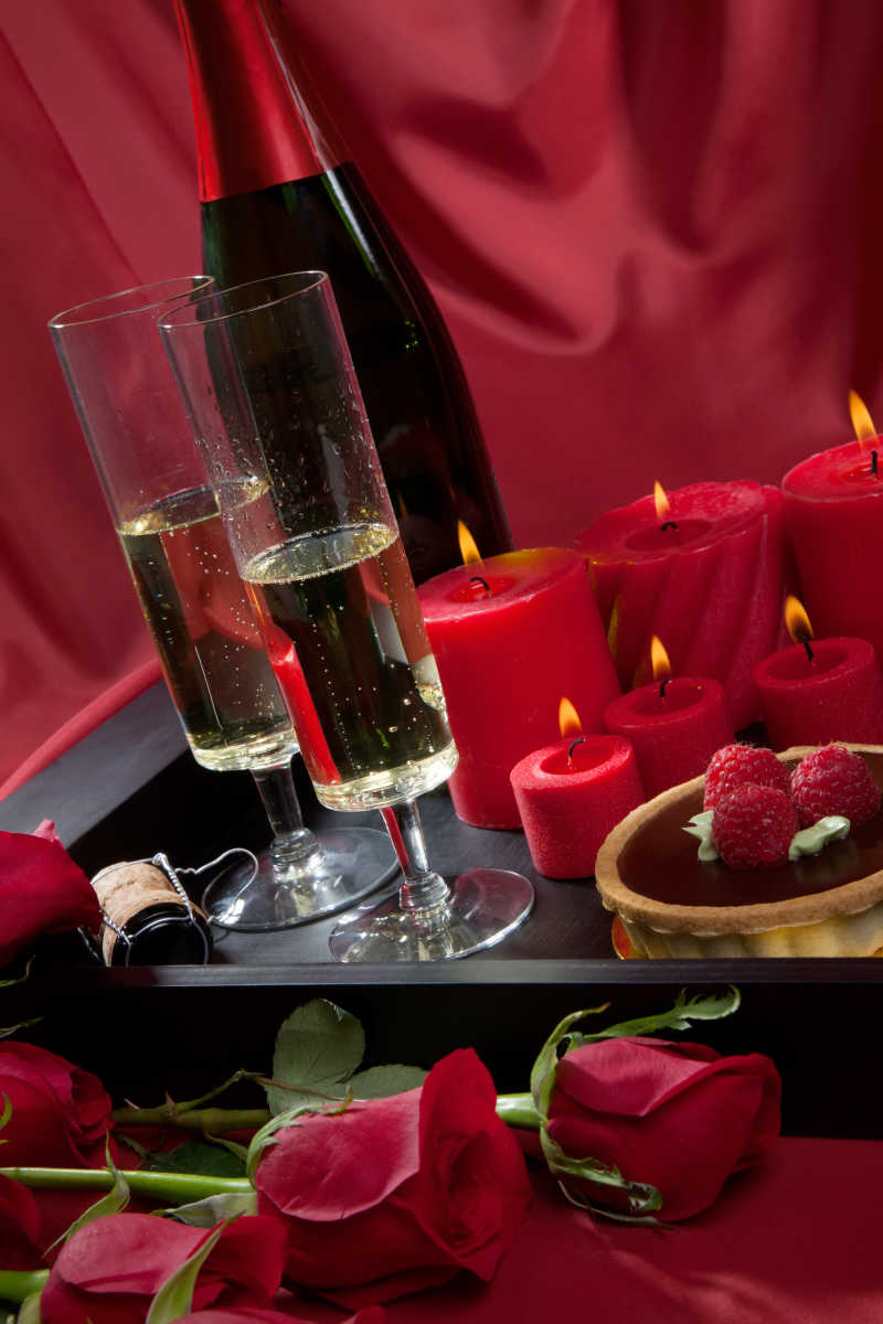  盘子里的香槟巧克力树莓蛋糕蜡烛和红玫瑰