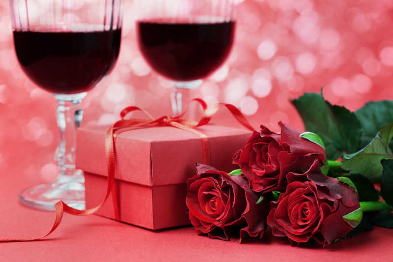 粉红色浪漫背景下的礼品盒红玫瑰花和两杯葡萄酒