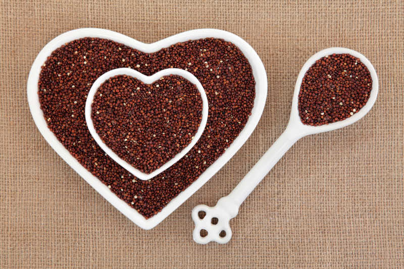 在黑森州的背景下的心形碗和瓷勺里的藜麦的超级食物