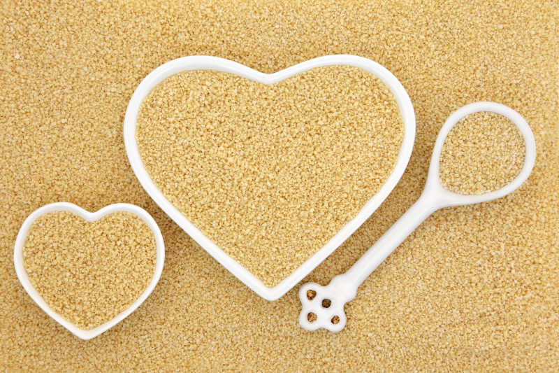 在心形碗和瓷勺形成背景蒸粗麦粉