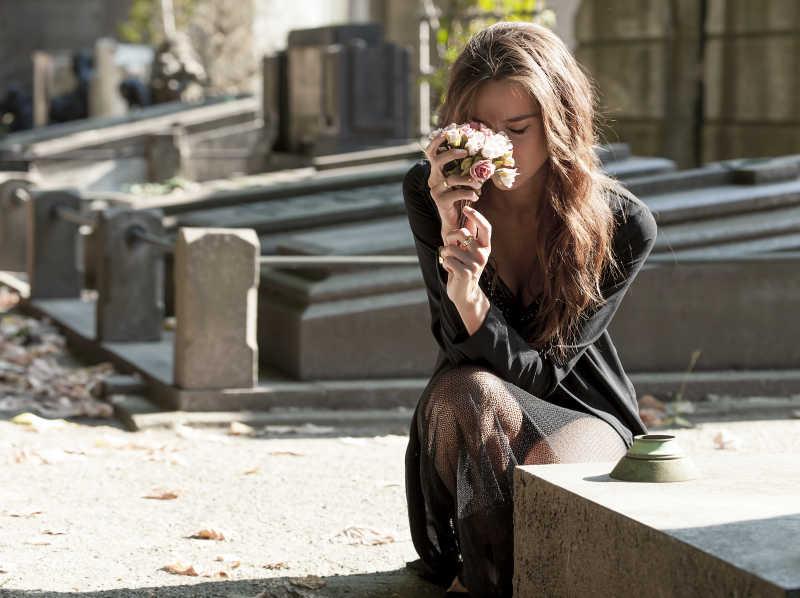 靠近坟墓的悲伤女人抱着一束花