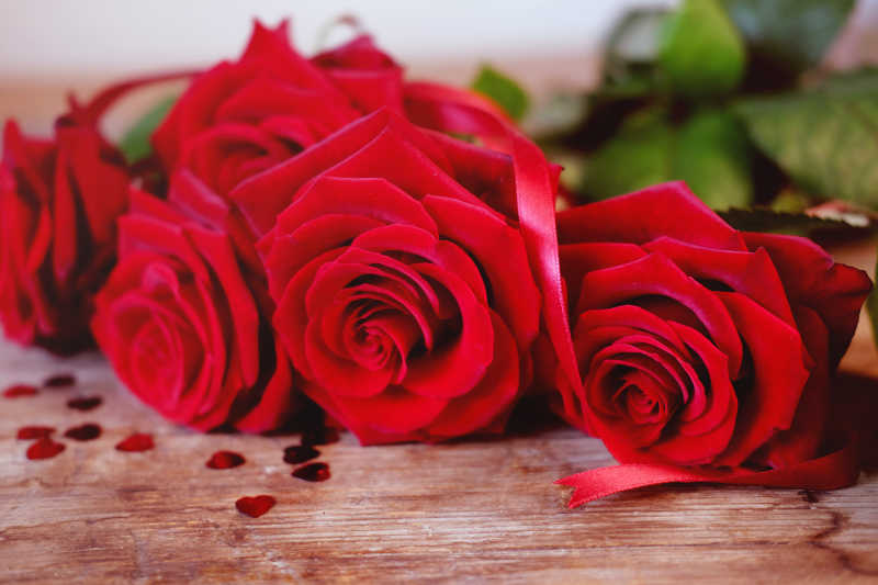 木桌上的红玫瑰花束和红色的丝带