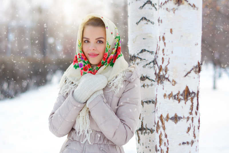 漂亮的美女在雪地里靠着树拍照