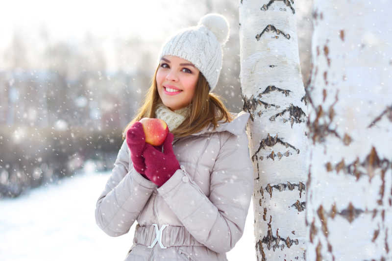 雪地里美女拿着苹果靠在树上