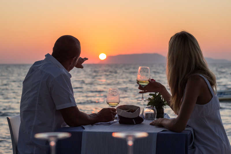 日落时分在海边餐厅拿着酒杯眺望海边日落的情侣