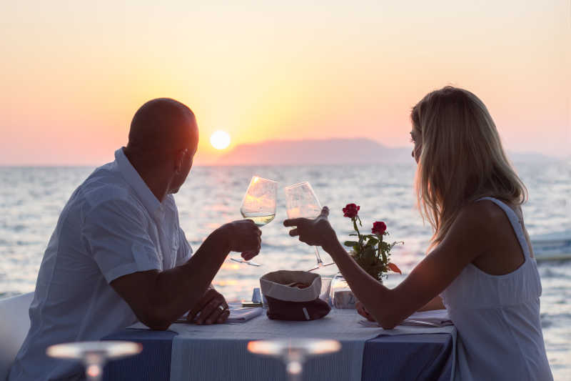 一对情侣在日落时分的海边餐厅对饮葡萄酒