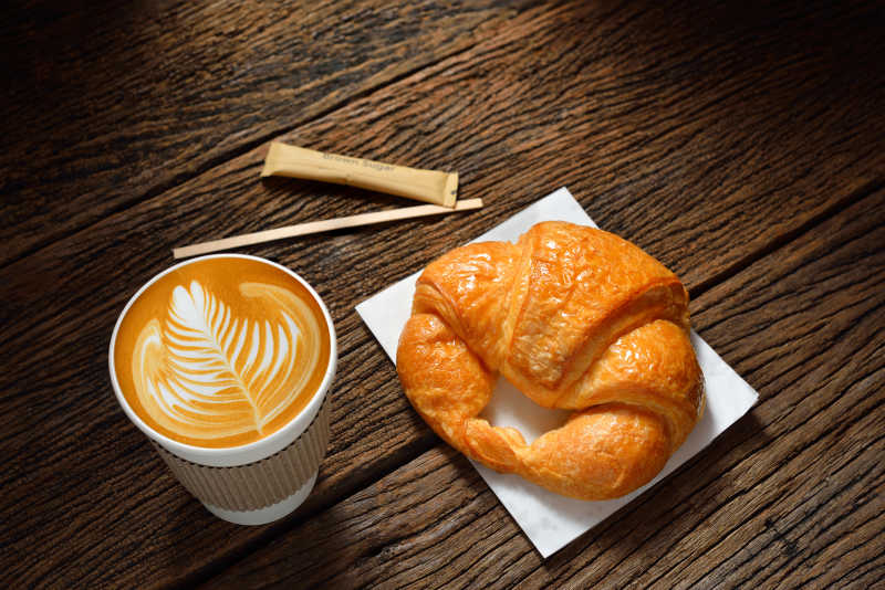 拿铁咖啡和牛角包旧木桌纸杯