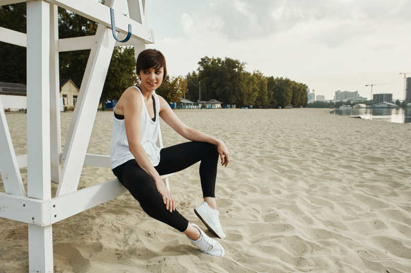 可爱的黑色运动装美女坐在沙滩上