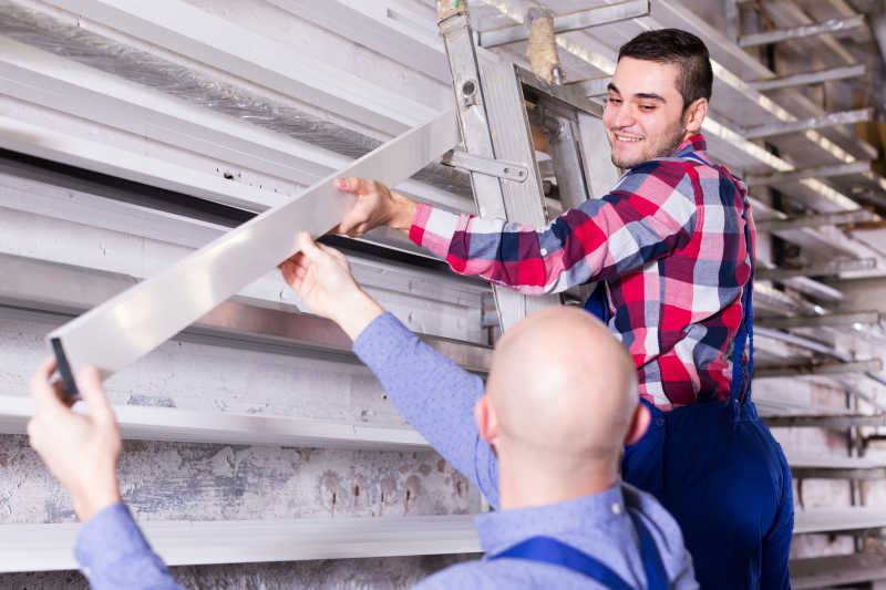 一名员工再给站在梯子上的工人递送窗框