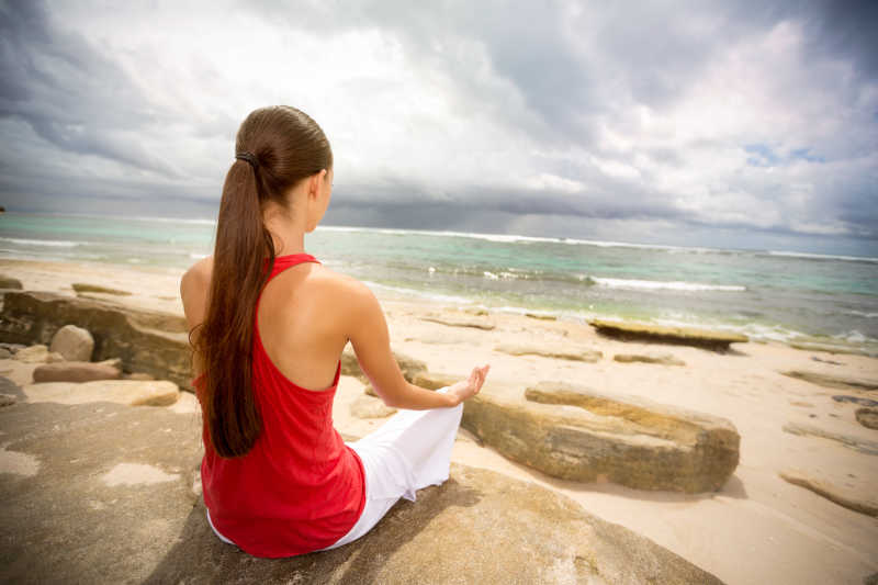 在海边沙滩岩石上打坐的年轻女人