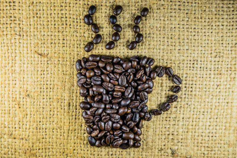 黄色亚麻布上咖啡豆摆出的热咖啡造型