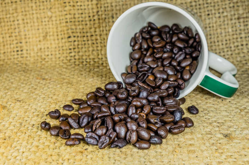 黄色亚麻布上杯子里倒出来的咖啡豆