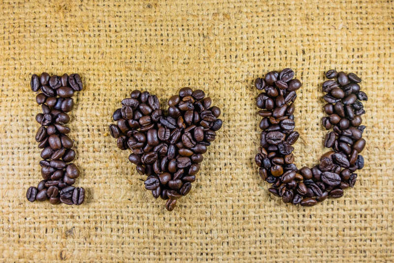 黄色亚麻布背景下咖啡豆组成的我爱你字母